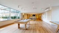 This 1340 square foot social hub, located at 533 Cottonwood Ave in Coquitlam, BC, is a testament to modern design and functionality. The single-floor space boasts an open-concept layout that seamlessly integrates various recreational areas. Floor-to-ceiling windows dominate one wall, flooding the interior with natural light and offering views of a manicured garden outside.

The hub features a game area with a stylish pool table and ping pong table, perfect for friendly competitions. Adjacent to this is a well-appointed kitchenette with sleek countertops and bar seating, ideal for casual dining or socializing. A separate dining area with a large wooden table and modern chairs provides a more formal eating space.

The lounge area is furnished with comfortable seating, including a plush sectional sofa and armchairs, centered around a wall-mounted flat-screen TV. Light wood flooring runs throughout, complementing the crisp white walls and creating a bright, airy atmosphere. Subtle design elements like wooden accent walls and contemporary artwork add visual interest.

Recessed lighting and cylindrical pendant lights contribute to the modern aesthetic while ensuring ample illumination. The space is climate-controlled with visible air conditioning units, ensuring comfort year-round. This versatile social hub is designed to accommodate various activities and gatherings in a stylish, contemporary setting.