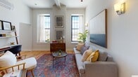 This thoughtfully designed single-floor residence offers a harmonious blend of classic architectural details and modern finishes throughout. Warm hardwood floors flow seamlessly across the living area, kitchen, and bedroom, creating a cohesive and inviting atmosphere.

The living room is a welcoming focal point, anchored by a large statement artwork and flanked by a pair of wall sconces that cast a warm glow. Multiple windows with black-framed trim flood the space with natural light and offer pleasant outdoor views, while high ceilings lend an open, airy quality to the room.

The kitchen is efficiently laid out with sleek grey cabinetry, white countertops, and stainless steel appliances, including a range and dishwasher. A pendant light above the sink adds a touch of character, and the space is designed to maximize both function and style.

The bedroom is a calm retreat, featuring a mini-split climate control unit for year-round comfort, a closet with a sliding door, and curated artwork that enhances the serene ambiance.

The bathroom is finished with dark hexagonal mosaic tile flooring, crisp white cabinetry, and clean white panel doors. A framed artwork and neatly hung towels complete the polished look, with a shower-tub combination rounding out the practical amenities.