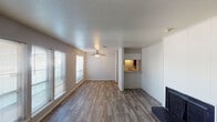 This single-floor residence offers a practical and comfortable layout designed for everyday living. The spacious living room serves as the heart of the home, showcasing rich wood-style plank flooring that extends throughout the main living areas. A standout feature is the floor-to-ceiling tiled fireplace surround, which anchors one wall and adds a classic focal point to the room. A ceiling fan with a light fixture provides both comfort and illumination, while multiple windows fitted with blinds allow natural light to fill the space. A pass-through opening connects the living area to the galley-style kitchen, which is equipped with dark cabinetry, laminate countertops, a coil-burner range, and a full-size refrigerator — all finished with the same wood-style flooring. The bedrooms are carpeted for warmth and comfort; one features a sliding door closet with built-in shelving, while another offers direct access to a bathroom. The bathrooms are finished with wood-style flooring and include essential fixtures. A textured ceiling throughout the main living space and neutral wall tones contribute to a clean, understated aesthetic that serves as a versatile canvas for any décor style.