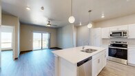 Located at 1439 Boardwalk Ave in Tiffin, Iowa, this well-appointed 2-bedroom, 3-bathroom unit offers a thoughtfully designed single-floor layout that balances functionality with modern style. Light-toned luxury vinyl plank flooring runs throughout, complementing the neutral warm-beige walls and dark baseboards found across every room.

The kitchen is a standout feature, showcasing crisp white shaker cabinetry, quartz countertops, stainless steel appliances including a range, microwave, and refrigerator, and a large center island with pendant globe lighting overhead — ideal for both meal prep and casual dining.

The living area is bright and open, with sliding glass doors leading to a private balcony that offers expansive open-field views. A ceiling fan adds comfort to the space. Both bedrooms are generously proportioned, each featuring large windows that frame the surrounding landscape, ceiling fans, and ample natural light. The spacious primary bedroom connects to a walk-in closet outfitted with wire shelving, which leads directly to a dedicated bathroom.

The three bathrooms are clean and modern, each with white cabinetry, quartz vanity tops, and vinyl plank flooring. One bathroom features a full soaking tub with shower and includes a convenient stacked in-unit washer and dryer. The overall ambiance is fresh, bright, and move-in ready.