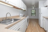 This single-floor residence at 1709 Cresthill Ave in Royal Oak, Michigan, offers a straightforward and functional layout designed for comfortable everyday living. The kitchen is equipped with white cabinetry extending to the ceiling, warm-toned laminate countertops, and a full suite of white appliances including an electric range, dishwasher, and refrigerator. Light hardwood-style flooring runs throughout the kitchen, which connects seamlessly to the main living area via a half-wall pass-through, enhancing the open feel of the space.

The living area is generously sized, finished with neutral wall-to-wall carpeting, and benefits from natural light through a window overlooking the outdoors. Bedrooms are carpeted as well, with one featuring a windowed wall that brings in additional daylight and another offering a built-in closet with bifold doors and dedicated storage space.

The unit includes two bathrooms: one with a tub-shower combination set in white square tile, and another with a separate walk-in shower stall fitted with grab bars, a vanity with an integrated sink, and stone-look tile flooring. Both bathrooms maintain a clean, bright aesthetic with white fixtures throughout.