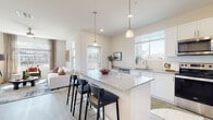 This modern single-floor home is thoughtfully designed with a clean, contemporary aesthetic throughout. The open-concept layout seamlessly connects the kitchen and living area, creating an inviting and functional space ideal for both everyday living and entertaining.

The kitchen is a standout feature, showcasing crisp white shaker cabinetry, light hardwood-style flooring, and a generously sized granite-topped island with seating for multiple guests, illuminated by elegant pendant lighting. A full suite of stainless steel appliances — including a refrigerator, range, microwave, and dishwasher — completes the space. Large windows flood the kitchen with abundant natural light.

The adjoining living room is bright and welcoming, featuring large windows that offer views of the surrounding neighborhood and allow natural light to pour in throughout the day. Neutral-toned walls and light flooring create a versatile backdrop for any décor style.

The bedroom is a serene retreat, carpeted for comfort and bathed in natural light from a large window with outdoor views. A ceiling fan adds practicality, and the room connects directly to a well-finished bathroom. The bathroom features white cabinetry, a granite vanity countertop, and clean, modern fixtures, maintaining the consistent design language found throughout the home. Overall, the space exudes a bright, airy, and move-in-ready appeal.