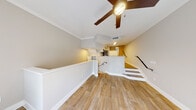 This thoughtfully designed single-floor residence offers a clean, modern aesthetic throughout its open and functional layout. The main living area greets you with warm wood-look luxury vinyl flooring, crown molding, and a ceiling fan, creating a bright and comfortable atmosphere. A sliding glass door opens onto a private balcony framed by a wrought-iron railing, flooding the space with natural light and offering pleasant views of lush surrounding greenery.

The kitchen is well-equipped and stylish, featuring white shaker cabinetry, a classic white subway tile backsplash, light quartz countertops, and a full suite of stainless steel appliances including a range, over-the-range microwave, and refrigerator. A deep stainless steel sink with a modern pull-down faucet completes the workspace. The kitchen is positioned at a split level and overlooks the main living area via a half-wall partition with additional white cabinetry, adding both storage and visual interest.

The staircase, finished with matching wood-look treads and white risers accented by a sleek black metal handrail, connects the living level to the lower level with an airy hallway leading to a private entry door. Additional rooms, finished in neutral tones with consistent flooring, provide versatile living spaces. The overall ambiance is clean, cohesive, and move-in ready.