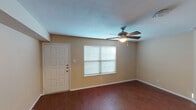 This single-story space offers a practical and cohesive layout designed for comfortable everyday living. The living area serves as the heart of the unit, featuring rich wood-look flooring that extends throughout the space, warm neutral-toned walls, and a textured ceiling fitted with a ceiling fan and light fixture. A front entry door and a window fitted with horizontal blinds allow natural light to fill the room, creating a bright and open atmosphere.

The kitchen is configured in a galley style, maximizing efficiency within a compact footprint. Dark espresso cabinetry lines both sides of the kitchen, complemented by granite-look countertops, a stainless steel double-basin sink, and black appliances including a refrigerator, electric range, and built-in microwave. Light wood-look flooring continues throughout this space, and a dedicated area accommodates a washer and dryer.

The bedroom is a well-proportioned room with the same wood-look flooring, a ceiling fan with light, and a window dressed with blinds that admits natural light. The bathroom includes a full tub-shower combination, a dark-cabineted vanity with a white countertop and single sink, a large mirror, and textured walls, completing the functional layout of this space.