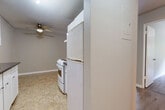 This 1-bedroom, 1-bathroom unit in Surrey, BC offers a practical and well-organized single-floor layout. The living room is the largest area of the unit, featuring light laminate wood flooring, neutral beige walls, baseboard heating, and a ceiling fan. Large sliding glass doors open to a private balcony, allowing natural light to fill the space and providing views of surrounding greenery. The kitchen is efficiently designed, tucked adjacent to the living area, and includes full-size white appliances — a refrigerator and electric range — set against tile flooring and a textured ceiling. A ceiling-mounted track light illuminates the kitchen zone. A hallway connects the main living spaces to the bedroom and bathroom. The bedroom is a comfortable, well-proportioned room with laminate flooring, a window overlooking greenery, a baseboard heater, and a built-in closet with bifold doors offering organized storage. The bathroom features tile flooring, a vanity with under-sink cabinet storage, a mirror with overhead lighting, and a tiled shower area. The unit also includes a dedicated closet for additional storage. Overall, the space presents a clean, functional layout with consistent neutral finishes throughout.