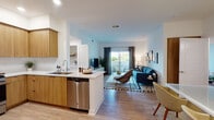 Located at 6450 Sepulveda Blvd in Los Angeles, this single-floor unit features a thoughtfully designed open-concept layout with contemporary finishes throughout. The kitchen is equipped with warm wood cabinetry, stainless steel appliances including a refrigerator, gas range, and microwave, complemented by a white quartz peninsula that flows seamlessly into the living area. Light wood-style flooring extends through the main living spaces, creating a cohesive and airy feel.

The living room receives natural light through a sliding glass door that opens onto a private balcony, offering outdoor views of surrounding greenery. The bedrooms are well-proportioned, featuring large windows with sheer curtains that allow ample natural light. One bedroom includes a mirrored sliding closet, while another offers a dedicated seating area. The bathroom is finished in crisp white tiling with a shower-tub combination and matching wood-tone flooring. A dedicated in-unit laundry closet houses a full-size GE washer and dryer with overhead shelving, providing practical storage. Recessed lighting throughout enhances the clean, modern aesthetic of this well-appointed space.