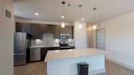 This single-floor residence features three bedrooms and two bathrooms within a thoughtfully designed open-concept layout. The kitchen serves as a central highlight, showcasing dark espresso cabinetry, granite countertops, a subway tile backsplash, and a full suite of stainless steel appliances including a refrigerator, range, microwave, and dishwasher. A large granite-topped island provides additional prep space and casual seating. Pendant lighting illuminates the kitchen, which flows seamlessly into the living area. The living space features light wood-style flooring, neutral walls, track lighting, and a window that allows natural light to fill the room.

The bedrooms are carpeted and equipped with ceiling fans, offering a comfortable and quiet retreat. Each room includes windows with exterior views. The primary bedroom connects to a private bathroom featuring a granite vanity with dark cabinetry, wood-style flooring, and access to a spacious walk-in closet with built-in shelving. The secondary bathroom includes a granite vanity, tub-shower combination with tiled surround, and matching wood-style flooring. The overall aesthetic is clean and contemporary throughout.