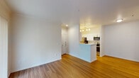 This single-story, one-bedroom, one-bathroom unit offers a functional and modern layout designed to maximize comfort and usability. The open-concept living area is finished with warm wood-style flooring that extends throughout the main living spaces, creating a cohesive and inviting atmosphere. A sliding glass door fitted with vertical blinds fills the living room with natural light while providing access to the outdoors.

The kitchen is positioned adjacent to the living area and features a peninsula-style breakfast bar that serves as a natural divider between the two spaces. White cabinetry with sleek hardware lines both sides of the galley-style kitchen, complemented by light countertops and a full suite of stainless steel appliances, including a refrigerator, range, microwave, and dishwasher. Pendant lighting above the peninsula adds a polished touch.

The bedroom is carpeted for added comfort and includes a ceiling fan with a light fixture, as well as a window with outdoor views and natural light. An adjoining bathroom offers wood-style flooring, a wide vanity with ample counter space, a large mirror, and access to a walk-in closet with built-in shelving, providing generous storage throughout.