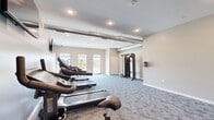 Located at 417 Karen Drive in Woodbury, MN, this dedicated fitness center offers a well-equipped exercise space designed to support a range of workout routines. The room is finished with patterned, low-pile carpet in neutral tones that complements the warm beige and soft teal accent walls, creating a clean and motivating atmosphere throughout.

The space is outfitted with multiple Spirit-brand treadmills and an elliptical machine, a stationary upright bike, and a multi-station cable strength-training system, providing options for both cardiovascular and resistance training. A wall-mounted flat-screen television is positioned for easy viewing during workouts. An exposed metal ductwork element along the ceiling adds an industrial design touch, while recessed lighting ensures the room is well lit at all times.

Large windows along one wall allow natural light to fill the space and offer views of an adjacent outdoor playground area, contributing to an open and energizing environment. A built-in water station with a drinking fountain and bottle-fill feature is conveniently mounted to the wall, supporting hydration during exercise. The fitness center is accessed through a glass-panel door and includes a dedicated thermostat for climate control, ensuring year-round comfort for users.