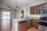 This single-floor unit is designed with a practical, open-concept layout that connects the kitchen and living area seamlessly. The kitchen is a standout feature, equipped with rich dark-wood cabinetry, granite countertops, a subway tile backsplash, and a full suite of stainless steel appliances including a range, microwave, and refrigerator. A central island with a dual-basin sink and pendant lighting above adds both functionality and visual interest. The living area extends naturally from the kitchen, featuring warm hardwood-style flooring, a ceiling fan, and access to a balcony that brings in natural light.

Two well-proportioned bedrooms each include ceiling fans, windows with outdoor views, and hardwood-style flooring. Both bedrooms offer generous closet space, with at least one featuring a walk-in closet outfitted with multi-tier wire shelving systems. The two bathrooms mirror the kitchen's design language, showcasing granite countertops, dark wood vanities, and hardwood-style flooring. One bathroom includes a tub-shower combination with tiled surround, while the other features a walk-in shower. Neutral gray walls throughout create a cohesive, calm ambiance across the entire unit.