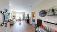 Located at 7027 Seguin Rd in San Antonio, Texas, this single-floor residence offers a thoughtfully arranged layout that balances comfort and functionality. The open living area is bathed in natural light from large windows dressed with sheer curtains, creating a bright and welcoming atmosphere. Rich wood-style flooring flows throughout the main living spaces, adding warmth and visual continuity.

The living room provides ample space for seating and entertaining, featuring neutral-toned walls that lend a calm, versatile backdrop. Adjacent to the living area, the kitchen is equipped with warm oak cabinetry extending to the upper walls, granite-style countertops, and a full suite of black appliances including a refrigerator, range, dishwasher, and microwave. A dining area sits just off the kitchen, completing the open common area.

The bedroom is a comfortable retreat with plush carpeting, a ceiling fan, and a window that allows natural light to filter in. It connects directly to a full bathroom outfitted with a combination tub and shower, wood-style flooring, and a vanity with under-sink storage. A spacious walk-in closet with built-in wire shelving provides generous storage. An additional utility closet with wire shelving offers even more organizational space, rounding out this practical and comfortable San Antonio residence.