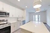 Located at 25 Silver Moon Circle in St. Augustine, FL, this thoughtfully designed single-floor residence offers a clean, modern aesthetic throughout. Light wood-style flooring runs continuously across the main living areas, complementing the bright white walls and creating a cohesive, airy feel.

The open-concept kitchen is a standout feature, boasting floor-to-ceiling white cabinetry, quartz countertops, a large center island, and a full suite of stainless steel appliances including a range, microwave, dishwasher, and refrigerator. Pendant lighting and recessed fixtures illuminate the space effectively. A pantry provides additional storage convenience.

The living room is welcoming and filled with natural light, featuring a ceiling fan and glass French doors that open to a private balcony with views of the surrounding greenery. The bedroom is a comfortable retreat with a large window overlooking the outdoors, a ceiling fan, and access to a spacious walk-in closet equipped with wire shelving. The bathroom includes a soaking tub with tile surround, quartz vanity, and tile flooring. Additional practical spaces include a laundry area, utility room, hallway, and entrance, rounding out the functional layout of this well-appointed residence.