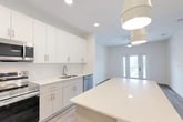 Located at 25 Silver Moon Circle in St. Augustine, FL, this thoughtfully designed single-floor residence offers a clean, modern aesthetic throughout. Light wood-style flooring runs continuously across the main living areas, complementing the bright white walls and creating a cohesive, airy feel.

The open-concept kitchen is a standout feature, boasting floor-to-ceiling white cabinetry, quartz countertops, a large center island, and a full suite of stainless steel appliances including a range, microwave, dishwasher, and refrigerator. Pendant lighting and recessed fixtures illuminate the space effectively. A pantry provides additional storage convenience.

The living room is welcoming and filled with natural light, featuring a ceiling fan and glass French doors that open to a private balcony with views of the surrounding greenery. The bedroom is a comfortable retreat with a large window overlooking the outdoors, a ceiling fan, and access to a spacious walk-in closet equipped with wire shelving. The bathroom includes a soaking tub with tile surround, quartz vanity, and tile flooring. Additional practical spaces include a laundry area, utility room, hallway, and entrance, rounding out the functional layout of this well-appointed residence.