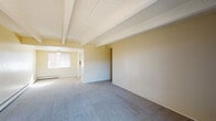 This single-floor residence offers a well-organized layout with a warm, neutral color palette throughout. The living areas are distinguished by textured ceilings accented with exposed structural beams, adding architectural character to the space. Soft blue-gray carpeting runs through the main living and bedroom areas, providing a comfortable underfoot experience.

The living room is generously proportioned, with a ceiling fan, a window fitted with blinds allowing natural light, and baseboard heating along the walls. Adjacent to the living area, the kitchen features white cabinetry, light countertops, warm terracotta tile backsplash details, and tile flooring. A full-size refrigerator is included, and a hallway connects to additional areas of the unit.

The bedrooms are notably spacious, each continuing the exposed beam ceiling design. Sliding glass doors in the bedroom open to a private balcony with a railing, offering striking views of surrounding mountains and mature trees — a standout feature of the space.

The primary bathroom is well-appointed with tile flooring, a wide vanity with white cabinetry, a large dark-framed mirror, a multi-bulb vanity light fixture, and a window for natural ventilation. A secondary half-bath provides additional convenience with a pedestal sink, mirror, and natural light from a small window. Baseboard heaters are present throughout, ensuring consistent warmth across all rooms.