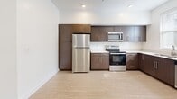 This 1-bedroom, 1-bathroom unit in Midvale, Utah offers a thoughtfully designed layout that maximizes every square foot. The kitchen is a standout feature, outfitted with rich dark-toned cabinetry, light countertops, and a full suite of stainless steel appliances including a refrigerator, range, microwave, and dishwasher. Natural light filters in through windows dressed with horizontal blinds, brightening the light wood-tone flooring that extends throughout the main living areas. A hallway connects the living spaces to the private quarters, featuring recessed lighting and clean white walls that lend a fresh, modern feel. The bedroom is carpeted for comfort and includes a ceiling fan with a light fixture, as well as a dedicated closet with double hanging rods — offering practical storage solutions. The bathroom is cleanly appointed with a full tub-shower combination featuring a curved curtain rod, a dark wood vanity with a white countertop, and tile-style flooring that ties the space together. Throughout the unit, crisp white walls, modern panel doors with brushed nickel hardware, and consistent finishes create a cohesive, contemporary aesthetic.