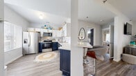 This well-appointed single-floor residence offers two bedrooms, one bathroom, and a thoughtfully designed layout that maximizes its comfortable footprint. The standout feature is the kitchen, which boasts a striking two-tone design with bold navy lower cabinets and crisp white upper cabinets, all accented by brushed gold hardware. Stainless steel appliances — including a refrigerator, range, microwave, and dishwasher — complement the clean white countertops and a gold-finished faucet. A peninsula with bar seating connects the kitchen to the open living area, creating an ideal space for entertaining. Light wood-look flooring runs throughout the main living areas, adding warmth and continuity. The living room is bright and welcoming, with a sliding glass door that invites natural light and provides outdoor views. The primary bedroom is a well-sized retreat with plush carpet flooring, soft neutral walls, and a window that fills the room with natural light. The second bedroom offers similar comfort and style. The bathroom features a clean, full-sized soaking tub and shower combination. Throughout the space, light-toned walls and consistent finishes create a cohesive, modern aesthetic.