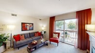 This thoughtfully designed 2-bedroom, 2-bathroom residence offers a comfortable and functional single-floor layout. The open-concept living, dining, and kitchen area forms the heart of the home, with plush carpeting and a ceiling fan throughout the main living space. The living room is bright and airy, highlighted by a large sliding glass door that opens to a private balcony overlooking a tree-lined outdoor area, filling the room with natural light. The kitchen features warm wood cabinetry, white appliances, a tile floor, ample counter space, and a breakfast bar that connects seamlessly to the dining area — ideal for both everyday meals and entertaining. The dining area accommodates a full-sized table and benefits from a ceiling fan overhead. The spacious primary bedroom includes a generous closet and is served by a well-appointed en-suite bathroom featuring a large vanity with extended counter space, a lighted mirror, and access to a second full bathroom complete with a tiled floor, vanity, and shower-tub combination. The second bedroom offers a comfortable retreat with natural light and carpeted flooring. A dedicated laundry area adds everyday convenience, rounding out this well-organized and inviting home.