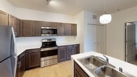 Located at 333 Nord Ave in Chico, California, this single-floor unit offers a thoughtfully designed layout with modern finishes throughout. The kitchen is a standout feature, showcasing rich dark cabinetry, stainless steel appliances including a refrigerator, electric range, and built-in microwave, all complemented by a white countertop island with a double sink and bar seating — ideal for casual dining or entertaining. Pendant globe lighting and a track light system illuminate the space with a warm, contemporary feel. Light wood-style flooring runs through the kitchen and living areas, adding continuity and brightness. The living room is cozy and functional, featuring a wall-mounted mini-split HVAC unit, natural light from a large window, and direct access to an outdoor patio through a glass door. The bedrooms are carpeted for comfort, each equipped with a ceiling fan and windows that bring in natural light. The bathrooms are finished with granite-style countertops, dark wood vanities, and a shower-tub combo, along with closet access for added convenience. Overall, the unit presents a clean, modern aesthetic with practical amenities suited for comfortable everyday living.