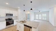 Located at 5801 Triangle Oaks Dr in Raleigh, NC, this well-appointed 2-bedroom, 2-bathroom residence offers a thoughtfully designed single-level layout with modern finishes throughout. The open-concept kitchen is a standout feature, showcasing a large granite-topped center island with an undermount sink, white shaker-style cabinetry, stainless steel appliances including a refrigerator, range, microwave, and dishwasher, and stylish pendant lighting overhead. Wood-look flooring flows through the kitchen and living areas, while recessed lighting and a ceiling fan enhance the bright, airy ambiance. The living area opens to a private balcony through glass-paneled French doors, inviting natural light and outdoor access. The bedrooms are carpeted and generously sized, each equipped with ceiling fans and ample natural light from large windows with blinds. The primary suite includes a spa-like ensuite bathroom featuring a double vanity with granite countertops, a frameless sliding glass shower, and direct access to a spacious walk-in closet with wire shelving. A second full bathroom and an additional walk-in closet with wire shelving provide functional storage throughout. The clean white walls and neutral palette create a bright, cohesive aesthetic across the entire residence.