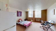 Located in Carbondale, IL, this single-floor studio unit offers a practical and efficiently organized layout well-suited for student or individual living. The main living area is generously proportioned, featuring wall-to-wall carpet flooring, a textured ceiling, and multiple large windows fitted with vertical blinds that allow ample natural light to filter throughout the space. A wall-mounted air conditioning unit provides climate control, and baseboard heating runs along the perimeter walls. The open layout accommodates both a sleeping area and a dedicated study or workspace, offering flexibility in how the room is arranged.

The kitchenette is situated along one wall and is equipped with white cabinetry, a dark laminate countertop, a double-basin sink, and a white electric range. Vinyl tile flooring defines this functional cooking area, and an adjacent closet with a curtained rod provides additional storage.

The bathroom is accessible via a private entry and includes a full-size bathtub with a shower and decorative curtain, a toilet, and a vanity sink. The combination of carpet and tile flooring throughout the unit adds a layer of warmth and practicality. Overall, this unit presents a straightforward, functional living environment in a convenient Carbondale location.