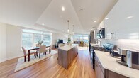 This thoughtfully designed single-floor residence showcases a seamless open-concept layout that connects the kitchen, dining, and living areas into one cohesive, light-filled space. Warm hardwood flooring runs throughout the main living areas, complementing the contemporary aesthetic. The kitchen is a standout feature, equipped with stainless steel appliances, two-tone cabinetry in white and wood-grain finishes, a subway tile backsplash, quartz countertops, and a central island with bar seating, illuminated by elegant pendant lighting. The dining area is bathed in natural light from large windows that frame expansive outdoor views of the surrounding cityscape and landscape. The living room extends this connection to the outdoors through a dramatic floor-to-ceiling window wall, filling the space with sunlight and panoramic views. A tray ceiling adds architectural depth to the main living zone. The bedroom offers a tranquil retreat with its own large window overlooking the urban skyline, along with a closet and plush flooring. The bathroom features clean tile flooring, a wide vanity with light wood cabinetry, and a frosted glass door leading to an adjacent space. The entry foyer provides a clean, modern welcome with a solid door and keypad access.