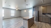 Located on Vin Etienne Drive in the 79912 zip code of El Paso, Texas, this single-story home showcases a cohesive modern design carried consistently throughout its interior. Large-format marble-look porcelain tile flooring flows seamlessly across every room, lending a clean and polished aesthetic to the entire space.

The kitchen serves as a centerpiece of the home, featuring granite countertops, a central island with pendant lighting overhead, flat-panel cabinetry in a warm taupe finish, a stainless steel farmhouse sink, and a full suite of stainless steel appliances including a refrigerator with ice and water dispenser, electric range, built-in microwave, and dishwasher. A geometric subway tile backsplash adds texture and visual interest behind the cooking area. Track lighting and pendant fixtures provide layered illumination throughout.

The open-concept living area adjoins the kitchen and benefits from multiple windows fitted with horizontal blinds, allowing ample natural light while maintaining privacy. Ceiling fans are installed in the main living areas and bedrooms, supporting comfort year-round. Additional rooms offer generous proportions, neutral wall tones, and consistent flooring. The bathroom features a glass-enclosed walk-in shower with decorative chevron tile accents and coordinating floor tile, completing the home's refined, contemporary finish.
