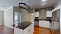 This single-floor, one-bedroom, one-bathroom residence offers a thoughtfully designed layout that maximizes its comfortable footprint. The open kitchen and living area serve as the heart of the unit, where warm hardwood flooring, crown molding, and neutral gray walls create a cohesive, modern aesthetic. The kitchen is well-equipped with a full suite of stainless steel appliances—including a refrigerator, range, microwave, and dishwasher—complemented by white shaker cabinetry, dark granite countertops, and a striking gray subway tile backsplash. A central island with additional storage and a suspended pot rack overhead adds both functionality and character. The living area benefits from natural light streaming through French doors fitted with white blinds and features a ceiling fan for year-round comfort. The bedroom is carpeted for warmth and includes a window with ample natural light. The full bathroom is finished with hardwood flooring, a dual-sink vanity with granite countertops, a soaking tub, and direct access to a dedicated walk-in closet outfitted with built-in shelving and hanging rods, providing generous storage throughout.