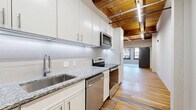 Located at 800 Broadway Blvd in the heart of Kansas City, MO, this one-bedroom, one-bathroom loft blends industrial character with contemporary updates. The open-plan kitchen and living area showcases the unit's most striking architectural feature: exposed wooden beam ceilings with tongue-and-groove wood paneling, lending warmth and a distinctly urban loft aesthetic. Reclaimed hardwood floors run throughout the main living spaces, adding texture and historic charm.

The galley-style kitchen is well-appointed with white shaker cabinetry, granite countertops, a subway tile backsplash, and a full suite of stainless steel appliances, including a range, microwave, dishwasher, and refrigerator. A sliding barn door separates the living area from the bedroom, reinforcing the industrial design theme.

The bedroom features plush carpeting, soft teal-toned walls, built-in closet storage with sleek panel doors, and multiple windows with bold dark frames that flood the room with natural light and offer views of the surrounding historic streetscape.

The bathroom includes a walk-in shower with white tile surround and modern chrome fixtures. The unit also includes a dedicated closet. Linear LED track lighting throughout complements the loft's modern-industrial character.