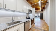Located at 800 Broadway Blvd in the heart of Kansas City, MO, this one-bedroom, one-bathroom loft blends industrial character with contemporary updates. The open-plan kitchen and living area showcases the unit's most striking architectural feature: exposed wooden beam ceilings with tongue-and-groove wood paneling, lending warmth and a distinctly urban loft aesthetic. Reclaimed hardwood floors run throughout the main living spaces, adding texture and historic charm.

The galley-style kitchen is well-appointed with white shaker cabinetry, granite countertops, a subway tile backsplash, and a full suite of stainless steel appliances, including a range, microwave, dishwasher, and refrigerator. A sliding barn door separates the living area from the bedroom, reinforcing the industrial design theme.

The bedroom features plush carpeting, soft teal-toned walls, built-in closet storage with sleek panel doors, and multiple windows with bold dark frames that flood the room with natural light and offer views of the surrounding historic streetscape.

The bathroom includes a walk-in shower with white tile surround and modern chrome fixtures. The unit also includes a dedicated closet. Linear LED track lighting throughout complements the loft's modern-industrial character.