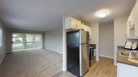 This single-floor unit offers a thoughtfully arranged layout that balances open living space with practical functionality. The living area is generously sized, finished with plush neutral carpeting and bathed in natural light through large vertical-blind-covered sliding glass doors that open to an outdoor view. A baseboard heating system runs along the perimeter walls, ensuring year-round comfort. Textured ceilings are consistent throughout the unit, adding a classic touch to the overall aesthetic.

The kitchen is efficiently designed with light wood-tone flooring, white cabinetry offering ample storage, dark countertops, and stainless steel appliances including a range and refrigerator. A sink with additional cabinet space completes the workspace.

The bedroom provides a comfortable retreat, featuring soft carpeting, a natural light-filled window with an outdoor view, and a full-width sliding-door closet offering generous storage. Baseboard heating is present here as well.

The bathroom is clean and well-appointed, featuring wood-tone flooring, a white vanity with a dark countertop, and a full tub-shower combination. The overall ambiance of the unit is bright, neutral, and move-in ready.