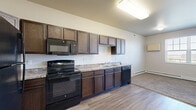 This studio apartment at 4551 47th Ave S in Fargo, North Dakota offers a well-designed, single-floor layout that makes efficient use of its compact footprint. The kitchen is a standout feature, equipped with dark espresso cabinetry, granite-style countertops, and a full suite of black appliances including an electric range, built-in microwave, dishwasher, and refrigerator. Wood-look vinyl flooring runs through the kitchen and living area, creating a clean, cohesive aesthetic. The living and sleeping area is carpeted and features a walk-in closet with wire shelving and hanging rods, providing ample storage. Two bathrooms serve the unit — one includes a stall shower alongside a stacked in-unit washer and dryer, offering the added convenience of private laundry. The second bathroom features a dark-cabinet vanity with a granite-style countertop and a large mirror. Neutral wall tones and consistent finishes throughout lend the space a tidy, move-in-ready feel. Natural light enters through windows in the main living area, complementing the ceiling-mounted lighting fixtures. A baseboard heating system ensures comfort year-round.
