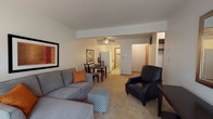 This single-floor residence is designed with a functional, open layout that connects the living, dining, and kitchen areas into one cohesive space. The living room is comfortably sized, featuring carpet flooring, a ceiling fan, and a large sliding glass door that floods the room with natural light and opens to a view of lush, mature trees. A side window further enhances the brightness and connection to the outdoors.

The dining area sits adjacent to the living room and flows directly into the galley-style kitchen. The kitchen is efficiently arranged with white appliances including a full-size refrigerator and gas range, ample cabinetry, a double stainless steel sink, and light vinyl flooring. A doorway from the kitchen provides additional access to the interior of the unit.

The bedroom is a tranquil retreat, benefiting from a wide, multi-pane window that frames a scenic wooded backdrop. It includes a wall-to-wall closet with sliding doors, carpet flooring, and a wall-mounted climate control unit. The full bathroom features a tiled tub-and-shower combination, a single vanity with under-sink cabinetry, and a medicine cabinet. Overall, the space offers a practical and comfortable layout with greenery views throughout.