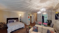 This single-floor studio offers a thoughtfully designed open-concept layout that efficiently combines living, sleeping, and dining areas into one cohesive space. Crown molding and hardwood-style flooring run throughout the main area, lending a polished, unified feel. Crystal-style pendant light fixtures add an elegant focal point overhead, while textured walls in the living area provide visual depth and character.

The sleeping and living zones flow seamlessly into one another, with ample room for a full-sized bed, seating, a dining area, and an entertainment setup. Natural light enters through a window dressed with patterned curtains, brightening the space during the day. A walk-in closet off the main area provides convenient storage.

The galley kitchen is well-equipped, featuring dark cabinetry, granite-look countertops, black appliances including a range and refrigerator, and a stainless steel sink—offering strong functionality within a compact footprint.

The bathroom includes a dark vanity with a granite-look countertop, a framed mirror with vanity lighting above, and hardwood-style flooring, creating a clean and cohesive finish consistent with the rest of the studio.