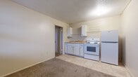 Located at 736 E 12th Ave in Emporia, Kansas, this efficient one-bedroom, one-bathroom unit offers a straightforward and functional layout across a single floor. The open-plan living and kitchen area features tile-style flooring that transitions into soft carpet, with a textured ceiling overhead. The kitchen is well-equipped with white cabinetry, a countertop sink, an electric range with oven, and a full-size refrigerator, making efficient use of the available space. Upper wall-mounted shelving provides additional storage. A doorway from the kitchen area leads to the bedroom and bathroom. The carpeted bedroom is a comfortable size, featuring a built-in closet with a hanging rod and shelf, offering practical storage solutions. Natural light enters through a window, giving the room a bright, airy feel. The bathroom is accessible directly from the bedroom and includes a wall-mounted sink and a stand-up shower stall with clean white surround panels. Throughout the unit, neutral wall tones and light-colored finishes create a clean, simple aesthetic. This unit is a practical option for those seeking straightforward, no-frills living accommodations in Emporia, KS.
