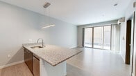 Located at 211 W Mineral St in Milwaukee's vibrant Walker's Point neighborhood, this modern one-bedroom, one-bathroom unit offers a thoughtfully designed, efficient layout with contemporary finishes throughout. Light wood-tone flooring flows seamlessly across the entire space, complementing the neutral gray walls and clean white trim.

The open-concept kitchen and living area forms the heart of the unit. The kitchen is equipped with stainless steel appliances, including a full-size refrigerator, microwave, and range, alongside crisp white cabinetry. A granite-topped peninsula island with an undermount sink and modern pendant lighting doubles as a breakfast bar, creating a natural transition into the living area. Sliding glass doors lead directly to a private patio, filling the space with natural light and providing outdoor access.

The bedroom is a well-proportioned, sunlit room featuring a large window with blinds overlooking the exterior, a sliding closet with wood-finish doors, and the same light flooring found throughout the unit. The full bathroom is cleanly finished with light wood-tone flooring, a soaking tub with shower, and multiple stainless grab bars for added accessibility. A dedicated laundry area rounds out the unit's practical amenities, making this a fully equipped, move-in-ready home.