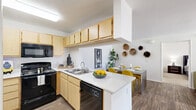 Located in Avondale, AZ, this single-floor 4-bedroom, 2-bathroom unit offers a practical and well-appointed layout. The open-concept living area features wood-look flooring, a ceiling fan, and a sliding glass door that fills the space with natural light and provides direct access to a private outdoor patio. The kitchen is equipped with light wood cabinetry, black appliances, a peninsula with a white countertop, and a double sink — flowing seamlessly into a dedicated dining area with recessed lighting and wood-look floors. The bedrooms are carpeted and include ceiling fans and windows that bring in natural light; the primary bedroom features a spacious layout with a large window overlooking a green outdoor view. Both bathrooms are finished consistently with wood-look flooring, light wood vanity cabinetry, white quartz countertops, and tiled shower-tub combinations. A dedicated laundry room houses a full-size side-by-side washer and dryer. Neutral white walls, consistent flooring materials, and a clean, cohesive design aesthetic are maintained throughout the unit. A hallway with carpet connects the bedrooms to the shared bathrooms, completing this functional and comfortable floor plan.