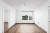 This single-floor unit presents a clean, modern aesthetic defined by crisp white walls, warm hardwood-style flooring, and a well-considered layout throughout. The open living area is a standout space, featuring a large picture window framing elevated views of a hillside cityscape, complemented by a ceiling fan overhead. Natural light flows generously into the room, enhancing its airy, open feel.

The kitchen is efficiently designed in a galley configuration, featuring light natural wood cabinetry, white countertops, stainless steel appliances including a dishwasher, and ample upper and lower storage. The layout maximizes functionality while maintaining a cohesive, minimalist appearance.

Multiple bedrooms are present throughout the unit, each finished with the same warm hardwood-style flooring and neutral white walls. Several bedrooms benefit from windows with outdoor views, while a ceiling fan provides additional comfort in the primary bedroom. A secondary bedroom offers a tall, narrow window admitting natural light.

The bathroom includes a full soaking tub with a clean white surround, brushed nickel hardware, and a simple, understated finish. The entry area provides a welcoming transition into the space, with clear sightlines connecting to the kitchen and living zones. Overall, the unit maintains a consistent, contemporary character throughout.