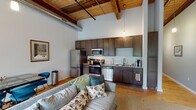 Located at 1151 Falls Rd in Rocky Mount, NC, this single-floor loft-style space showcases a striking blend of industrial character and modern comfort. Dramatic soaring ceilings with exposed wooden beams and visible ductwork define the open living area, which is bathed in natural light streaming through large multi-pane windows fitted with roller shades. Hardwood floors run throughout, anchoring the warm, industrial aesthetic.

The open-concept kitchen is thoughtfully appointed with dark espresso cabinetry extending to ceiling height, granite countertops, a classic white subway tile backsplash, and a full suite of stainless steel appliances including a range, microwave, dishwasher, and refrigerator. A pendant light fixture adds a refined industrial touch overhead.

The spacious living area accommodates generous seating and a dining space, with exposed concrete block walls adding authentic loft character alongside the wood-paneled ceiling details.

The primary bedroom features soaring ceilings, hardwood floors, and direct access to a private en-suite bathroom finished with a marble-topped vanity and a tiled walk-in shower. A secondary bedroom with classic hardwood floors offers dual twin beds with decorative headboards. The clean, well-appointed bathroom rounds out this thoughtfully designed urban loft retreat.
