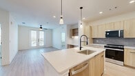 Located at 4205 McEwen Rd in Farmers Branch, TX, this well-designed 2-bedroom, 2-bathroom residence offers a thoughtfully planned single-level layout with a clean, contemporary aesthetic throughout. Light wood-style flooring runs seamlessly across the entire space, complementing the bright, neutral palette of crisp white walls and warm natural tones.

The open-concept kitchen and living area serves as the heart of the home. The kitchen is outfitted with flat-front light wood cabinetry, a subtle gray tile backsplash, stainless steel appliances including a refrigerator and range, and a large central island with a white countertop and integrated sink — finished with sleek matte black fixtures. Pendant lighting above the island adds a modern touch, while recessed lighting ensures the space is well-illuminated throughout.

Both bedrooms are bright and spacious, each featuring ceiling fans and large windows that invite natural light and offer views of the surrounding area. One bedroom includes French doors opening to a private balcony. Each bedroom is served by a dedicated bathroom, with one featuring a soaking tub and tiled shower surround, and both include walk-in closets with built-in shelving and hanging rods for ample storage.

The overall ambiance is modern, clean, and move-in ready, with consistent finishes that create a cohesive and inviting living environment.