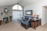This single-floor residence at 26598 E Carnegie Park Drive in Southfield, Michigan, is defined by its dramatic vaulted ceilings, which rise prominently in the living and dining areas, creating an airy, open atmosphere. The living room is a standout space, anchored by a fireplace and a striking arched window that floods the room with natural light. Sliding glass doors with vertical blinds provide access to the outdoors, further enhancing the sense of openness. Soft carpeting throughout the main living areas adds warmth and comfort.

The dining area sits beneath a pendant light fixture, with the vaulted ceiling continuing overhead and a pass-through shelf connecting to the kitchen. The kitchen features wood-trimmed white cabinetry, laminate countertops, full appliances including a range and refrigerator, and hardwood-style flooring.

The bedrooms are carpeted and well-proportioned, each with windows allowing natural light. One room functions effectively as a home office or flex space, equipped with a ceiling fan. The bathroom includes a vanity with wood cabinetry, tile flooring, and a glass-enclosed shower. A walk-in closet provides additional storage. Overall, the space offers a functional and comfortable layout with notable architectural character.