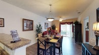 This single-floor residence at Blankenbaker Crossings offers a thoughtfully designed open layout that connects the main living areas seamlessly. The living room serves as a welcoming central space, featuring wood-style flooring, a ceiling fan, and a large sliding glass door dressed with decorative drapery that floods the room with natural light and provides direct access to an outdoor patio with exterior views.

The dining area sits adjacent to the living room, anchored by a pendant light fixture overhead and positioned conveniently near the kitchen. The kitchen is efficiently arranged with warm wood cabinetry extending to the upper walls, granite-style countertops, and black appliances including a range, microwave, and refrigerator, all set on durable wood-style flooring.

The bedroom is a calm, carpeted retreat featuring a ceiling fan with light kit, large windows dressed with layered valances that bring in generous natural light, and ample space for furnishings. The textured ceiling carries throughout the unit, adding a consistent design element across all rooms.

The bathroom offers a practical layout with a dark wood vanity, a wide mirror with overhead lighting, wood-style flooring, and a tub and shower combination, completing this well-rounded and functional residence.