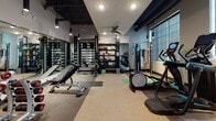 Located at 530 Meeting St in Charleston, SC, this modern fitness center is a well-appointed, single-floor facility designed to support a wide range of workout routines. The space features durable rubberized flooring throughout and is illuminated by a combination of recessed lighting and sleek pendant fixtures suspended from an exposed dark-painted ceiling with visible ductwork, lending the space an industrial-contemporary aesthetic.

The cardio zone is positioned along a wall of large grid-pane windows, flooding the area with natural light. It is equipped with multiple treadmills, elliptical machines, and a stationary bike, each featuring integrated digital screens. A ceiling fan overhead enhances airflow across the workout floor.

The strength training area offers a comprehensive selection of free weights, adjustable dumbbells, and weight benches, supported by floor-to-ceiling mirrors that amplify the sense of space. A well-stocked equipment rack holds medicine balls, resistance bands, and various accessories for functional training. A cable and resistance machine system rounds out the strength options.

A dedicated boxing corner features a freestanding Everlast heavy bag, offering space for combat fitness and high-intensity interval training. The facility is well-organized and thoughtfully zoned, providing an efficient, professional-grade workout environment suitable for all fitness levels.