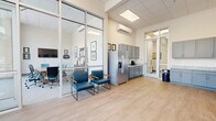 Located at 462 Cherry Street in downtown Macon, Georgia, this single-floor commercial office space offers a well-appointed and functional layout designed for professional use. The building's striking exterior features floor-to-ceiling glass walls that flood the welcoming lobby and common areas with abundant natural light, offering open views of the surrounding streetscape and mature trees. The lobby area is finished with light hardwood-style flooring and accommodates casual seating and high-top tables, creating an inviting reception atmosphere.

The space includes four private offices, each outfitted with L-shaped wood-finish desks and carpeted flooring, providing a clean and productive work environment. A dedicated conference room features a wall-mounted display, a large conference table, and teal upholstered seating, complemented by expansive windows with views to the exterior. Two connecting hallways efficiently link the various rooms throughout the suite.

The kitchen is well-equipped with granite countertops, gray shaker-style cabinetry, a stainless steel refrigerator, and light hardwood-style flooring. An adjacent breakroom area extends the kitchen's functionality with additional cabinetry, a printer station, and access to the exterior. The overall design is modern, clean, and professional, making this space well-suited for a variety of business operations.