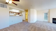 The Windom is a well-appointed 1-bedroom, 1-bathroom unit designed for comfortable, efficient living on a single floor. The living area greets residents with plush carpeting, a ceiling fan with light fixture, and a classic fireplace that serves as a focal point of the room. A door leads to an outdoor area, allowing natural light to filter in and providing convenient exterior access. The kitchen features warm wood-toned cabinetry, white appliances including a refrigerator, electric range, and over-the-range microwave, along with hard surface flooring and a pass-through counter that connects to the main living space. The bedroom is a quiet retreat with soft carpeting, a broad window fitted with vertical blinds for natural light control, and ample wall space for flexible furniture arrangements. The bedroom also includes a spacious walk-in-style closet outfitted with built-in shelving and a hanging rod, offering excellent organization potential. The bathroom is clean and functional, featuring a full tub-shower combo with tile surround, and hard surface flooring. Throughout the unit, neutral wall tones and consistent finishes create a cohesive, move-in-ready atmosphere.