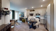 Located at 11001 W 15th Pl in Lakewood, Colorado, this single-floor residence offers a thoughtfully designed open-concept layout that seamlessly connects the kitchen, dining, and living areas. The kitchen is equipped with stainless steel appliances, including a range, microwave, dishwasher, and refrigerator, complemented by light wood-tone cabinetry, a built-in wine rack, and clean white countertops. Wood-look flooring flows throughout the main living areas, adding warmth and continuity to the space. The dining area accommodates an intimate round table setup, while the living room features a bold deep-green accent wall, recessed lighting, and ample room for comfortable seating. Natural light filters in through multiple windows dressed with blinds and curtain panels. The bedroom continues the nature-inspired green color palette with plush carpeting, a ceiling fan, and generous window placement that enhances the sense of openness. The bathroom is finished with warm wood-tone cabinetry, a wide vanity with a large mirror, and a walk-in shower with tiled surround. Additional storage is thoughtfully integrated throughout. This residence combines modern finishes with cohesive design elements for a comfortable and visually engaging living environment.
