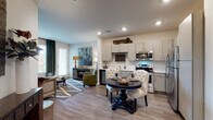 Located at 11001 W 15th Pl in Lakewood, Colorado, this single-floor residence offers a thoughtfully designed open-concept layout that seamlessly connects the kitchen, dining, and living areas. The kitchen is equipped with stainless steel appliances, including a range, microwave, dishwasher, and refrigerator, complemented by light wood-tone cabinetry, a built-in wine rack, and clean white countertops. Wood-look flooring flows throughout the main living areas, adding warmth and continuity to the space. The dining area accommodates an intimate round table setup, while the living room features a bold deep-green accent wall, recessed lighting, and ample room for comfortable seating. Natural light filters in through multiple windows dressed with blinds and curtain panels. The bedroom continues the nature-inspired green color palette with plush carpeting, a ceiling fan, and generous window placement that enhances the sense of openness. The bathroom is finished with warm wood-tone cabinetry, a wide vanity with a large mirror, and a walk-in shower with tiled surround. Additional storage is thoughtfully integrated throughout. This residence combines modern finishes with cohesive design elements for a comfortable and visually engaging living environment.