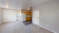 Located at 1300 Renshaw Rd in Chester, Pennsylvania, this single-floor unit offers a practical and straightforward layout designed for comfortable everyday living. The kitchen serves as a central hub of the space, equipped with warm honey-toned wood cabinetry, a gas range with a ventilation hood, a tiled backsplash, and a full-size refrigerator. Dark tile flooring grounds the kitchen area, which flows seamlessly into the adjoining carpeted living spaces. The generously sized main living area features soft wall-to-wall carpeting, neutral gray walls, a paneled ceiling, and multiple windows fitted with blinds that allow for natural light. Baseboard heating runs along the perimeter, ensuring warmth throughout. Additional rooms, each finished with the same neutral carpeting and gray tones, offer versatile space suitable for bedrooms or flexible use, with windows providing views of the surrounding greenery. The full bathroom includes classic turquoise tile surround in the tub and shower area, a mosaic tile floor, a vanity, and a toilet — giving it a retro charm. The overall ambiance is clean, neutral, and move-in ready, offering a functional and well-organized living environment.