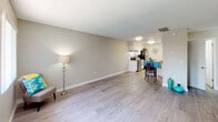 This single-story residence at 730 Via De Luna in Corona, California, offers a well-organized layout with a cohesive, modern aesthetic throughout. The living area is open and inviting, featuring durable wood-look laminate flooring, neutral-toned walls, and a textured ceiling that adds subtle depth to the space. Large windows with vertical blinds allow ample natural light to fill the room, creating a bright and comfortable atmosphere. The front entry opens directly into this living space, which flows seamlessly toward the kitchen and dining area. The kitchen is well-appointed with white cabinetry, light granite-style countertops, a classic white subway tile backsplash, a double-basin stainless steel sink, and stainless steel appliances including a range and refrigerator. A dishwasher is also included. Adjacent to the kitchen, a cozy dining nook accommodates a small round table, making it a practical space for everyday meals. The bedroom features plush carpeting, a window with vertical blinds that brings in natural light, and neutral walls offering a calm retreat. The bathroom is clean and functional, equipped with white cabinetry, a vanity with a granite-style countertop, a tub-shower combination, and wood-look flooring. A dedicated closet with shelving is conveniently located directly adjacent to the bathroom, providing practical storage solutions throughout the unit.