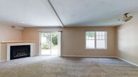 Located at 110 Brook View Dr in North Kingstown, Rhode Island, this two-floor home offers a well-organized layout with comfortable living spaces throughout. The main level centers around a generously sized living room featuring plush carpeting, a corner fireplace, and vaulted ceilings with exposed beams that add architectural character. Sliding glass doors flood the room with natural light and provide direct access to the backyard, where mature greenery creates a private outdoor setting. A secondary window further brightens the space. The kitchen is outfitted with white cabinetry, ample counter space with neutral-toned laminate countertops, a double sink, dishwasher, and warm hardwood flooring. A half bathroom on the main level includes a white vanity, oval mirror, and tile flooring. The attached garage features a concrete floor and an automatic opener, offering convenient interior access. Upstairs, the bedrooms are carpeted and benefit from vaulted ceilings and natural light from multiple windows. One bedroom features a spacious walk-in closet with wire shelving, while another includes a double-door closet. A full bathroom upstairs is appointed with tile flooring, a walk-in shower, and a white vanity. Throughout, warm neutral tones create a cohesive and inviting ambiance.