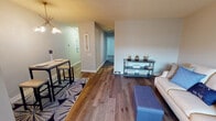 This single-floor residence offers a thoughtfully designed layout that maximizes functionality and comfort. The open-concept living and dining area serves as the heart of the home, featuring warm hardwood-style flooring that flows seamlessly throughout the main living spaces. The living room provides ample space for relaxing and entertaining, with a large window that allows natural light to fill the room, neutral-toned walls, and room for a full sofa and accent seating. A dedicated dining area sits adjacent, complete with a bistro-style table and pendant lighting overhead.

The kitchen is well-equipped for everyday cooking, featuring white cabinetry, granite-look countertops, and stainless steel appliances including an electric range with a ventilation hood. A hallway connects the main living areas to the private quarters of the home. The bedroom offers a calm, carpeted retreat with soft, neutral walls and enough space to comfortably accommodate a full-sized bed and additional furnishings. The full bathroom includes wood-style flooring, a toilet, and a tub/shower combination, finished with clean, neutral tones that contribute to a fresh and functional feel. Overall, the space presents a comfortable and move-in-ready environment.